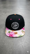 Black cap with floral brim and brand logo on a gray surface